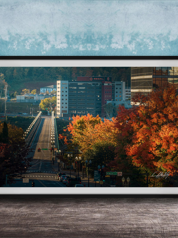 a cityscape with a bridge, buildings, and trees with autumn foliage.