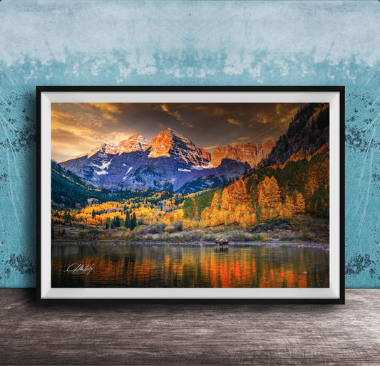 The image is a framed photograph depicting a scenic mountain landscape with a lake in the foreground, surrounded by trees with autumn foliage.