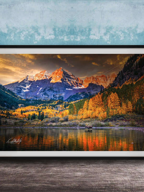 The image is a framed photograph depicting a scenic mountain landscape with a lake in the foreground, surrounded by trees with autumn foliage.