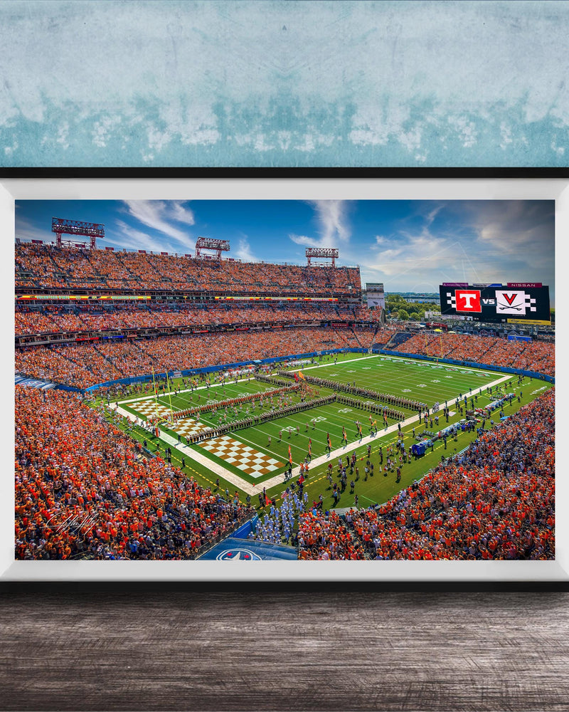A framed photograph of a crowded football stadium during a game, with the field and stands filled with spectators.