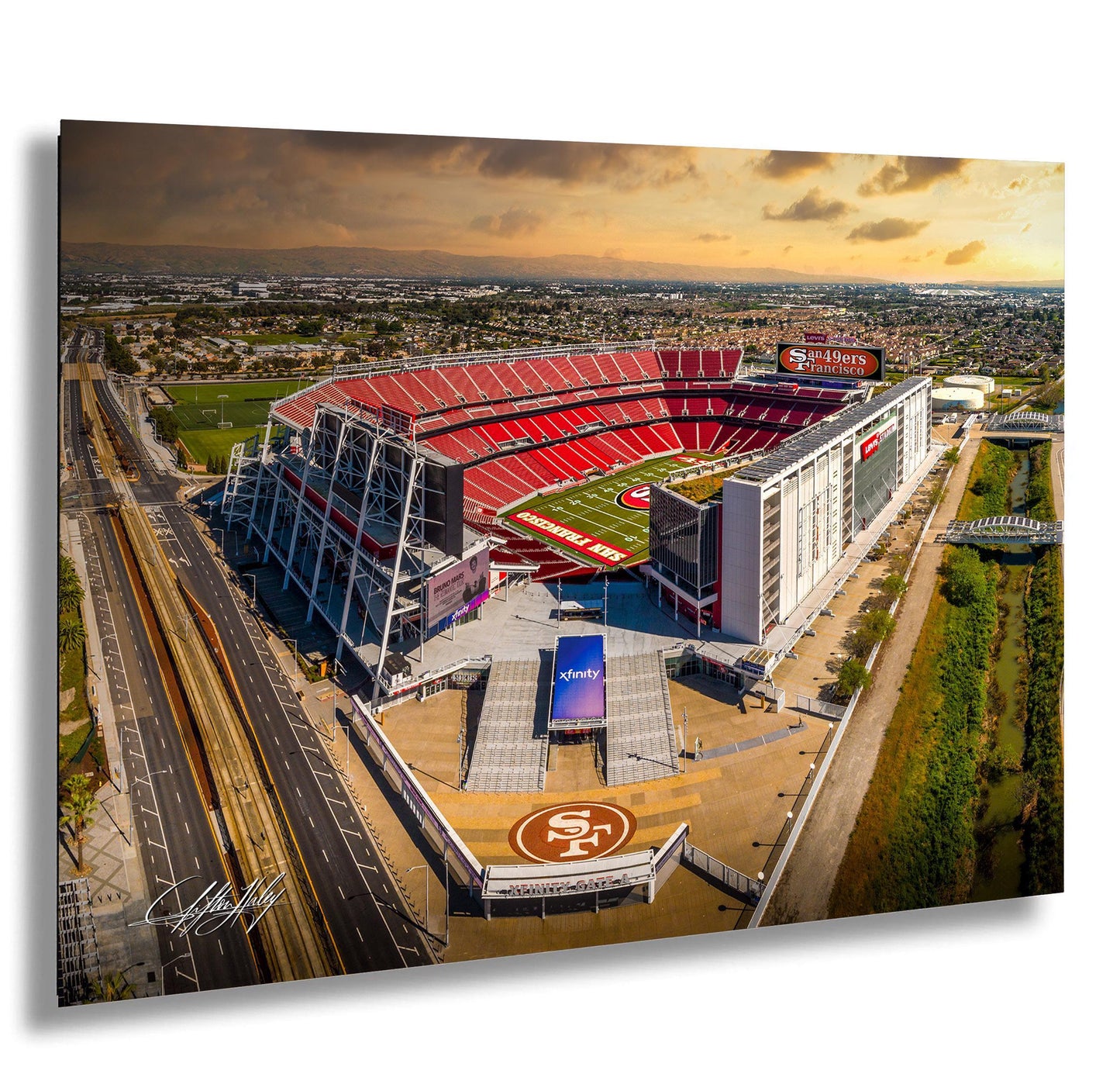 An aerial view of a large sports stadium, likely the San Francisco 49ers stadium, with the surrounding cityscape and a cloudy sky in the background.