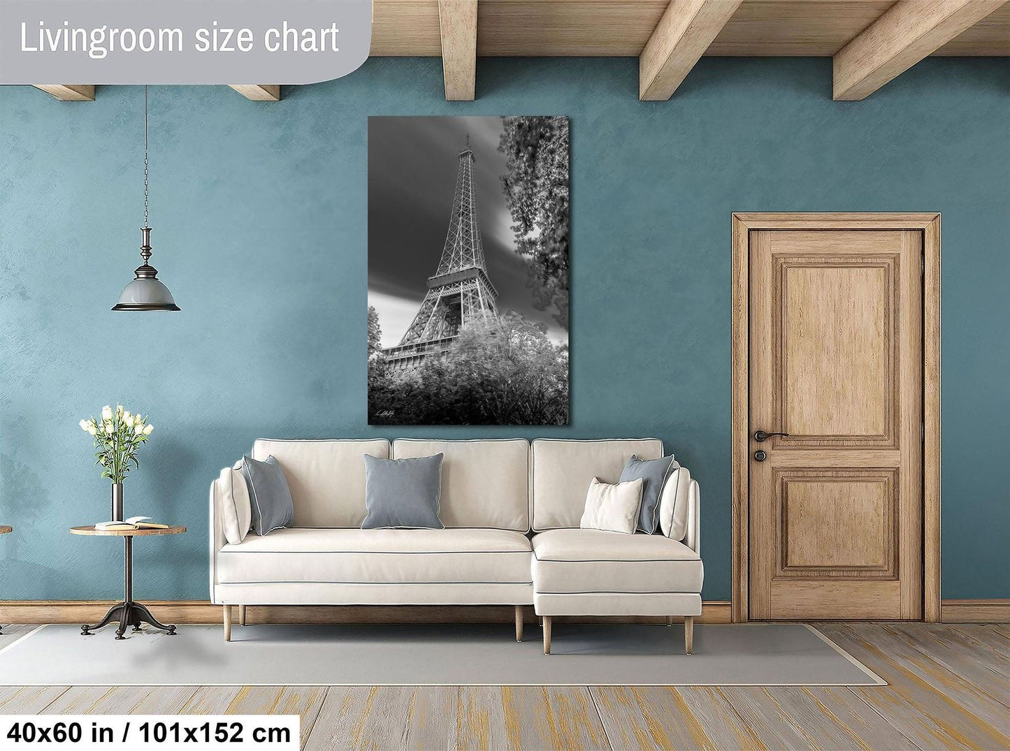 a living room with a large black and white photograph of the Eiffel Tower hanging on the wall. The room has a white sofa, a wooden door, and a wooden table with a vase of flowers. The living room appears to be well-lit and spacious, with a large window providing natural light.