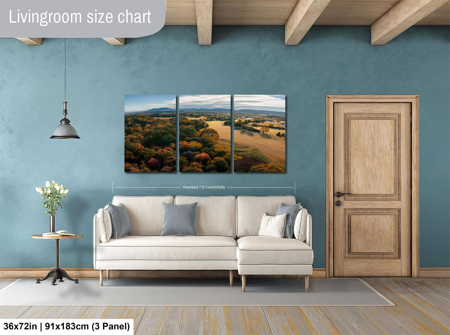 The image is a living room with a large wall art depicting a scenic landscape. The living room has a white sofa, a wooden door, and a wooden floor. The wall art is a collage of three panels, each depicting a different aspect of the landscape. The wall art is approximately 36 inches wide and 11 inches tall, and it is mounted on a blue wall.