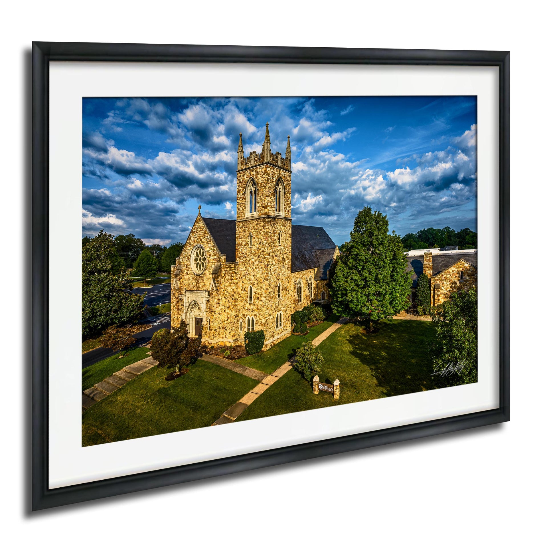 A stone church with a tall tower and a clock, surrounded by trees and a grassy area, set against a blue sky with clouds.