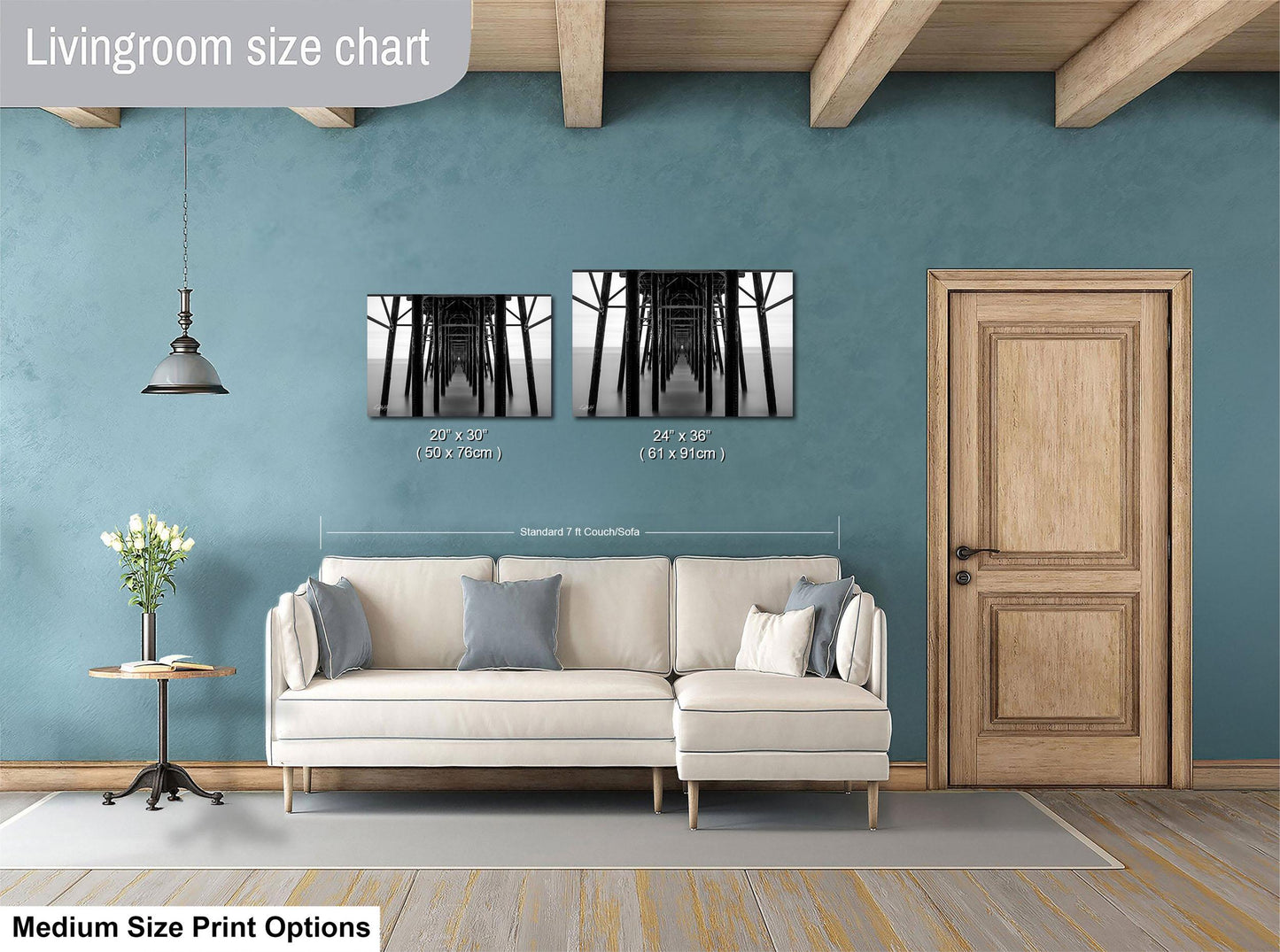 a living room with a white sofa, a wooden door, and a potted plant. There are two framed black and white photographs hanging on the wall, one above the other. The wall has a blue color, and the floor is covered with a rug.