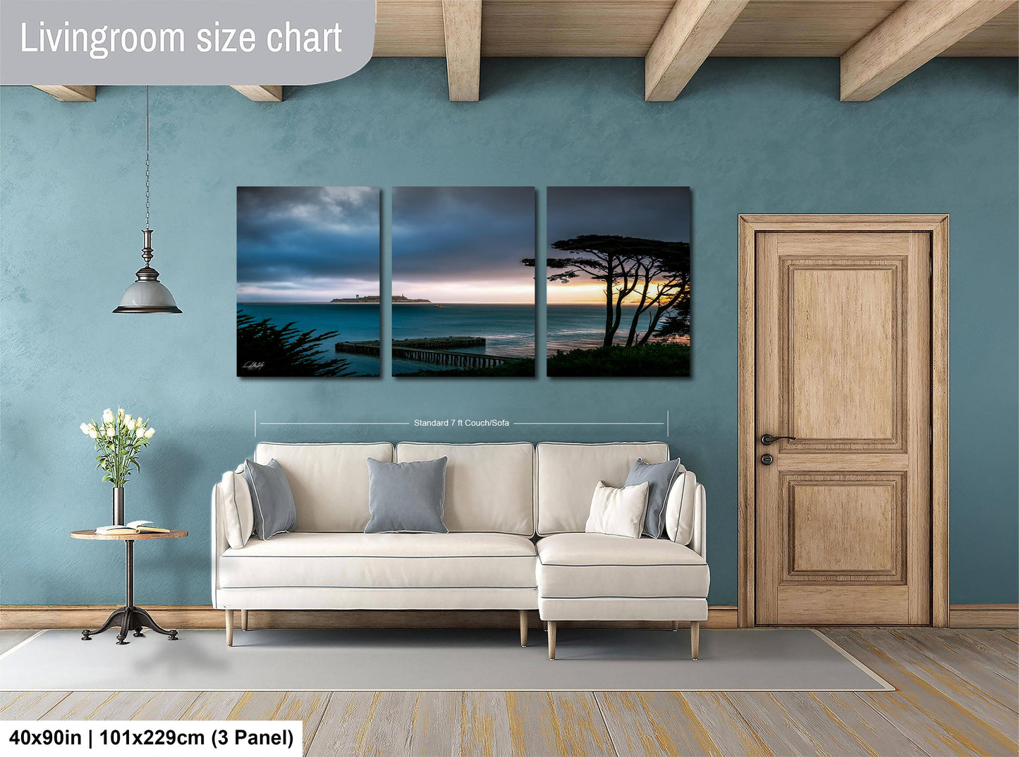 The image is a living room with a large wall art piece depicting a serene landscape of a beach at sunset. The art piece is divided into three panels, each showcasing different aspects of the beach scene. The living room has a white sofa and a wooden door, creating a cozy and inviting atmosphere.