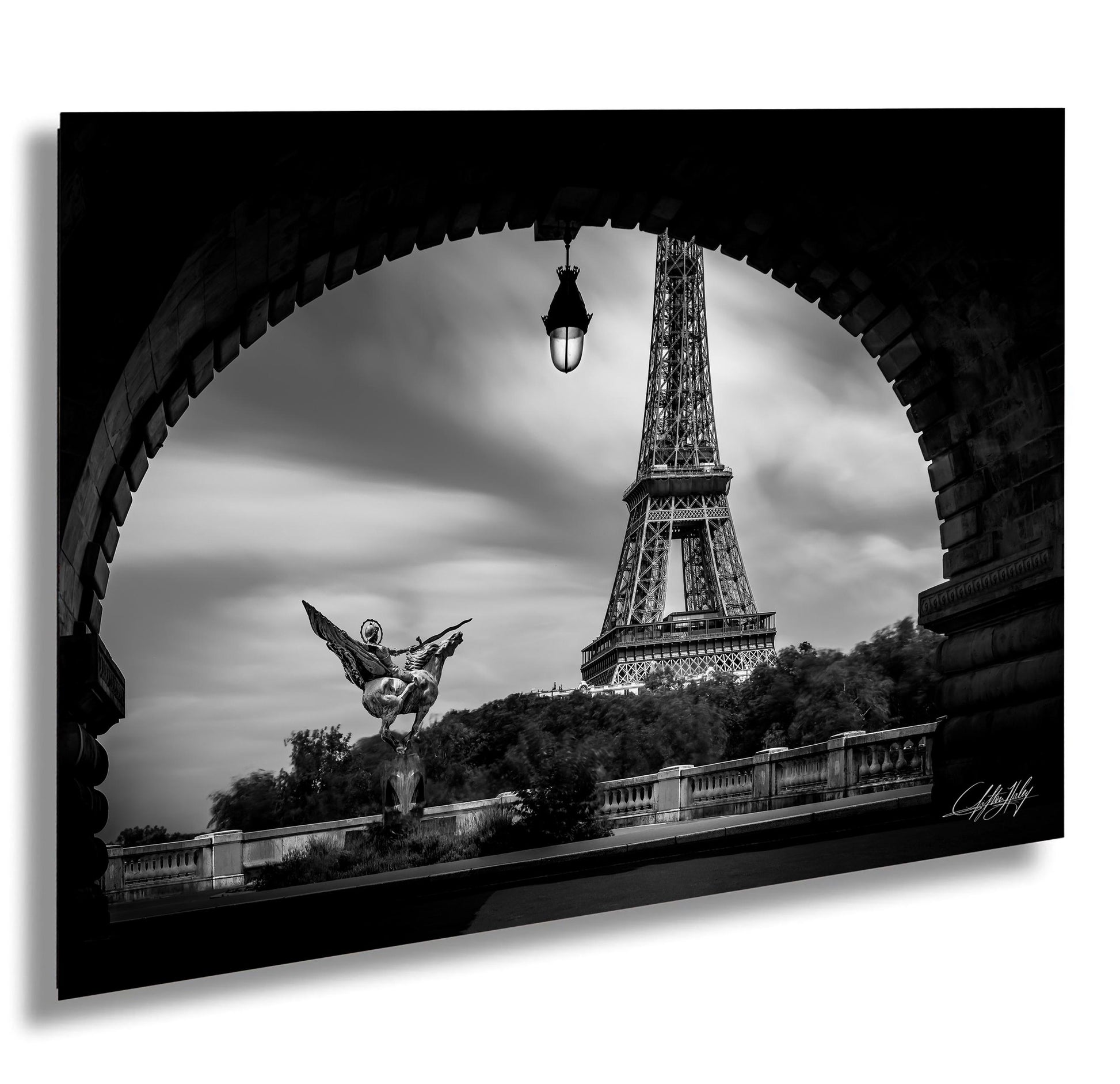 A black and white photograph of the Eiffel Tower in Paris, France, with a statue of a winged figure in the foreground and a stone archway framing the scene.