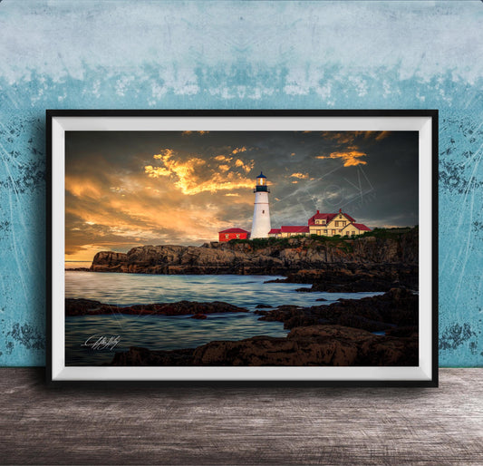 A framed photograph depicting a lighthouse on a rocky coastline at sunset, with the sky filled with clouds and the ocean in the background.