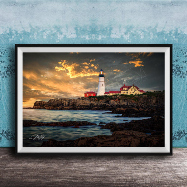 A framed photograph depicting a lighthouse on a rocky coastline at sunset, with the sky filled with clouds and the ocean in the background.