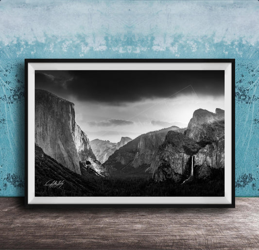 A black and white photograph of a mountainous landscape, with dramatic clouds and a waterfall in the foreground.