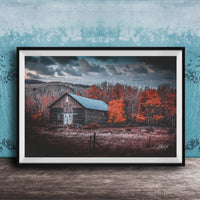 A rustic wooden barn stands in a field, surrounded by trees with vibrant orange leaves against a cloudy sky.