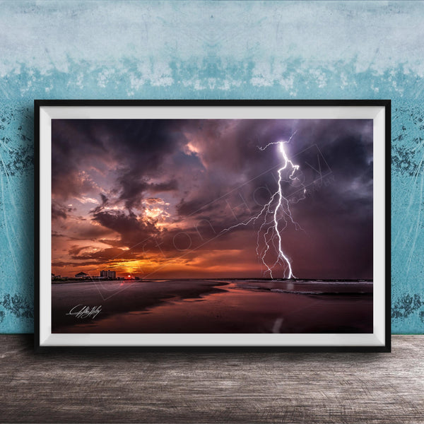 A framed photograph depicting a dramatic lightning storm over a beach at sunset, with the sky filled with vibrant colors and the lightning bolt striking the horizon.