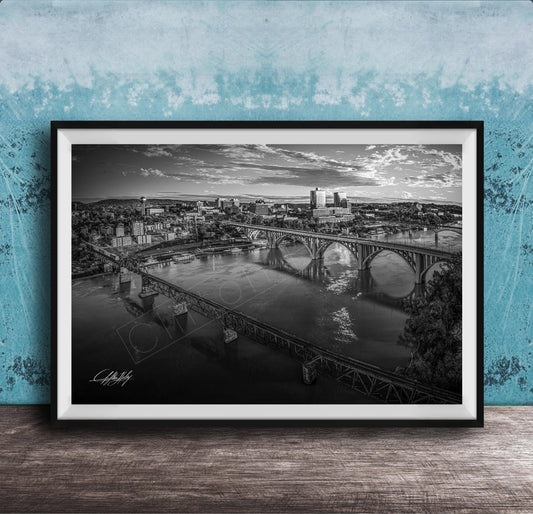A black and white aerial photograph of a cityscape with a large bridge spanning a river, set against a blue textured wall.