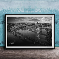 A black and white aerial photograph of a cityscape with a large bridge spanning a river, set against a blue textured wall.