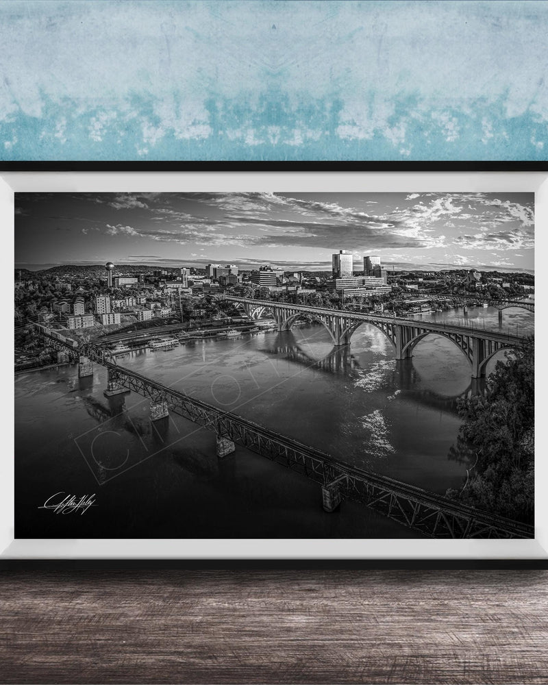 A black and white aerial photograph of a cityscape with a large bridge spanning a river, set against a blue textured wall.