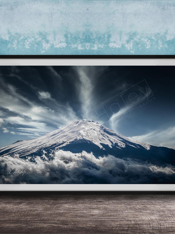A framed photograph of a snow-capped mountain peak, with dramatic clouds and a dramatic sky in the background.