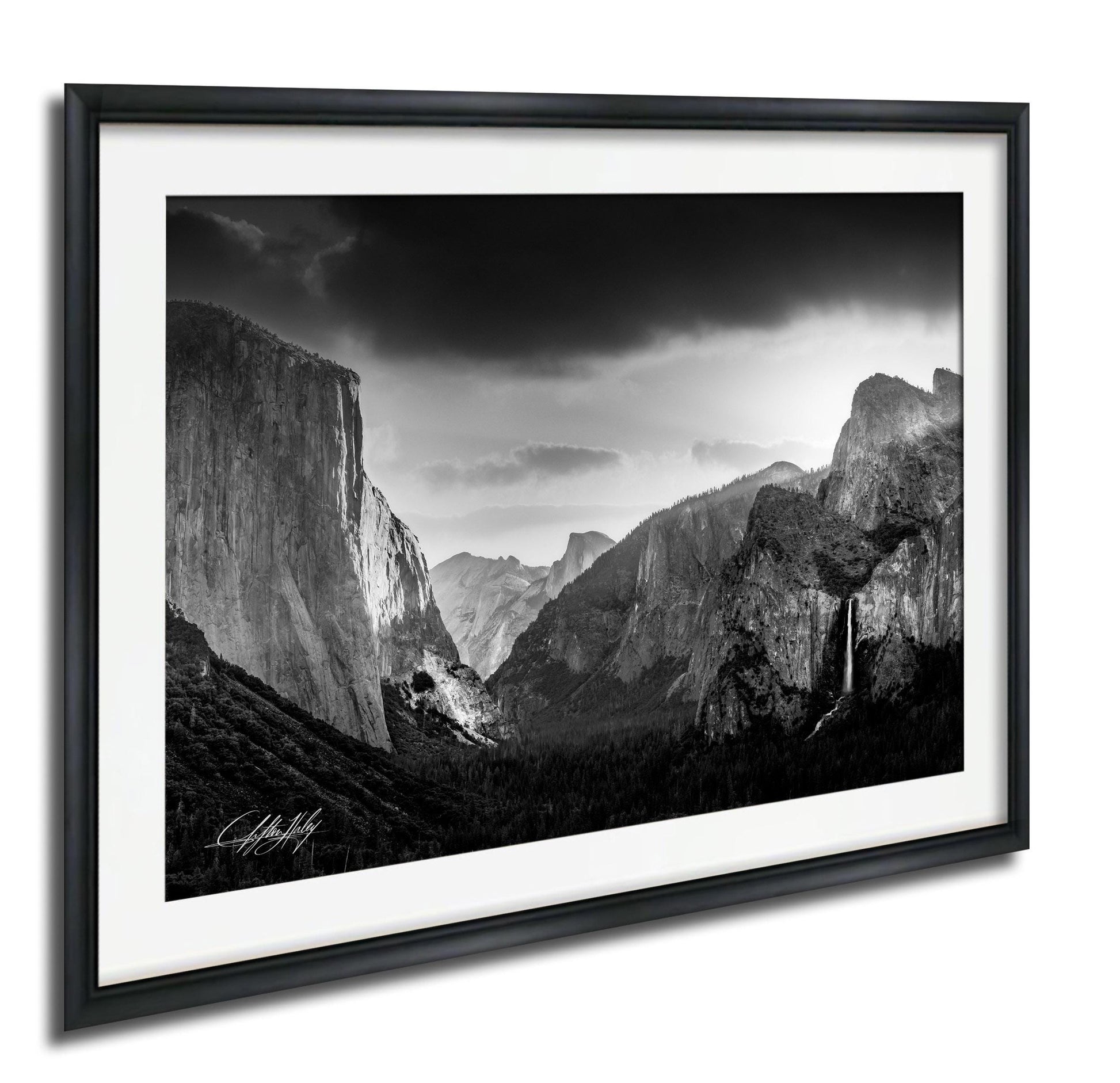 A black and white photograph of the majestic Yosemite Valley, with towering cliffs and a dramatic sky in the background.