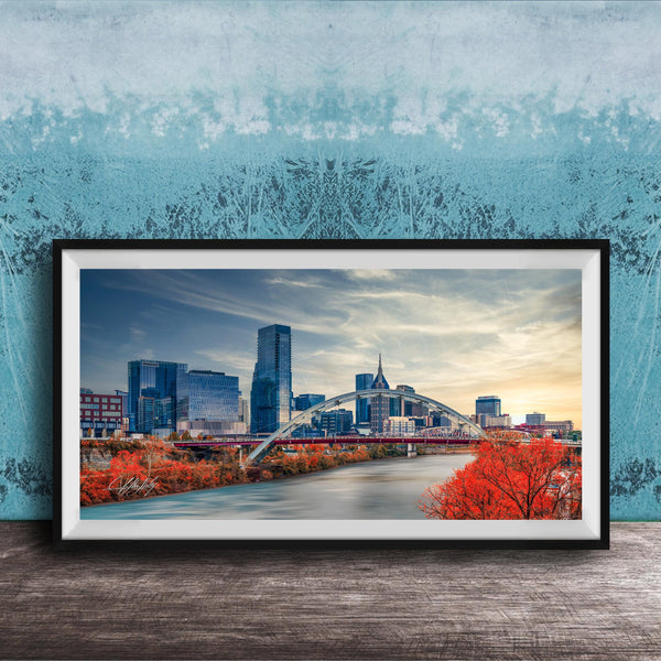 a framed photograph of a city skyline with a bridge and trees in the foreground.