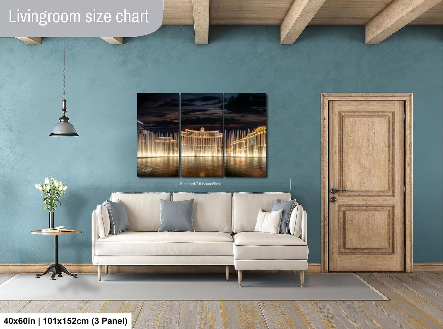 The image is a living room with a white sofa, a wooden door, and a large wall art depicting a nighttime cityscape with illuminated buildings.