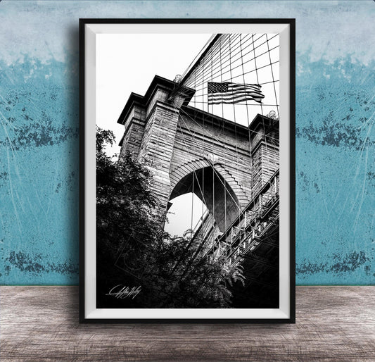 A black and white photograph of a brick bridge with an American flag flying above it, set against a blue textured background.
