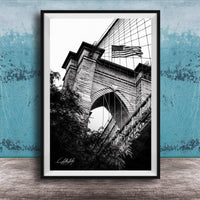 A black and white photograph of a brick bridge with an American flag flying above it, set against a blue textured background.