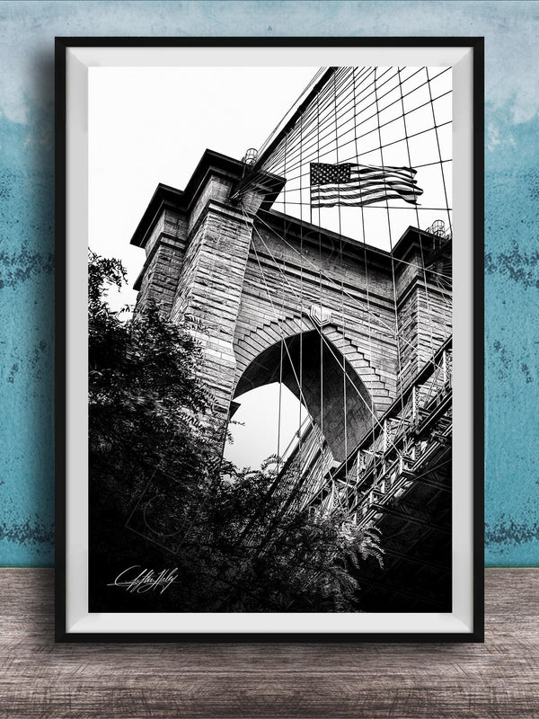 A black and white photograph of a brick bridge with an American flag flying above it, set against a blue textured background.