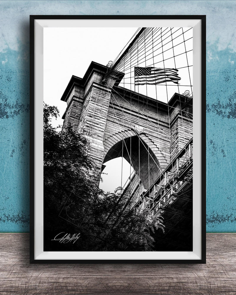 A black and white photograph of a brick bridge with an American flag flying above it, set against a blue textured background.
