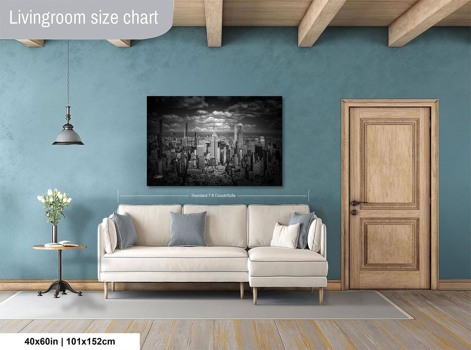 a living room with a large cityscape painting hanging on the wall. The painting is framed in black and white and measures 40 inches by 101.5 centimeters. The room has a white sofa, a wooden door, and a small table with a vase of flowers.