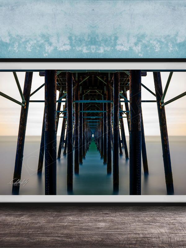 The image is a framed photograph of a long pier with multiple wooden columns extending into the distance, creating a sense of depth and perspective.