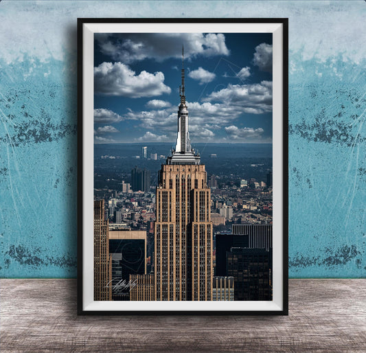 A framed photograph of the iconic Empire State Building in New York City, with the cityscape of Manhattan visible in the background.