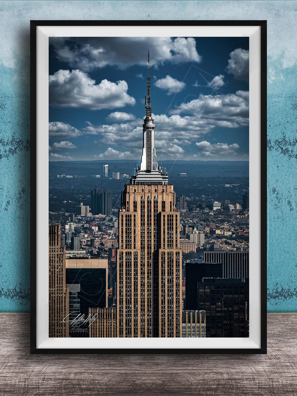 A framed photograph of the iconic Empire State Building in New York City, with the cityscape of Manhattan visible in the background.