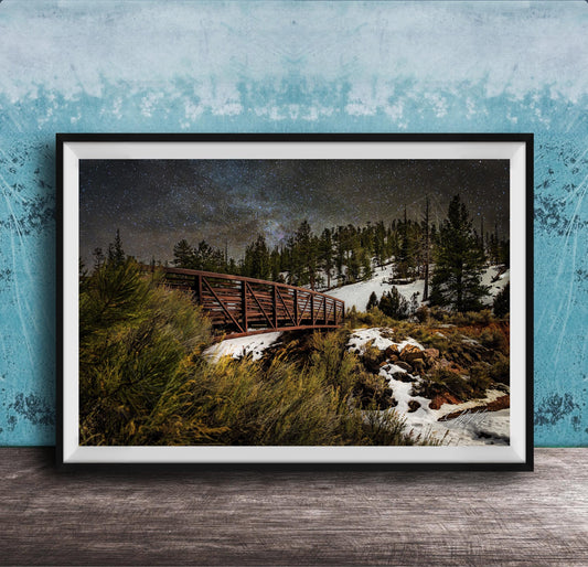 A framed photograph depicting a wooden bridge crossing a snowy mountain landscape at night, with a starry sky overhead.