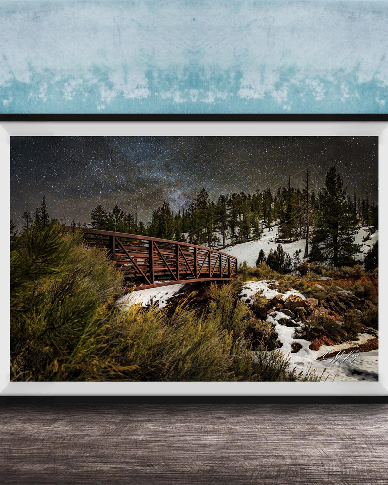 A framed photograph depicting a wooden bridge crossing a snowy mountain landscape at night, with a starry sky overhead.