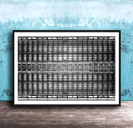 The image is a framed black and white photograph of a grid-like structure, possibly a building or a machine, set against a blue textured wall.