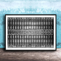 The image is a framed black and white photograph of a grid-like structure, possibly a building or a machine, set against a blue textured wall.