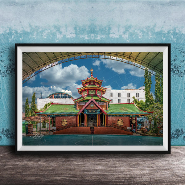 A framed photograph of a traditional Chinese temple with a red roof and green walls, set against a blue sky with clouds.