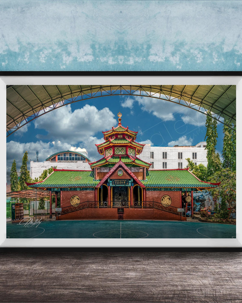 A framed photograph of a traditional Chinese temple with a red roof and green walls, set against a blue sky with clouds.