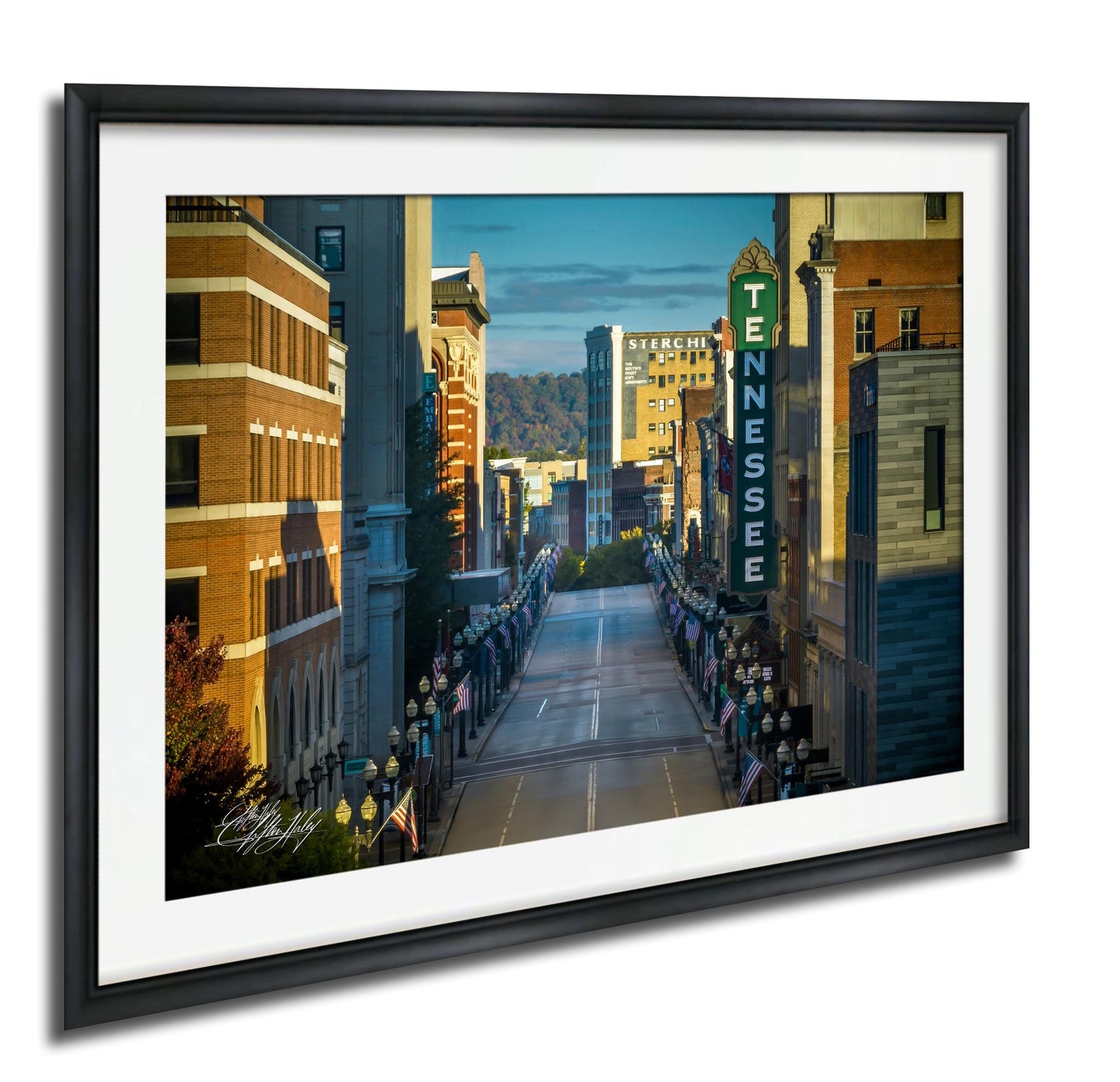 a city street lined with tall buildings, including a prominent sign for "TENNESSEE" on the right side. The street is decorated with numerous American flags, suggesting a patriotic or celebratory atmosphere. The overall scene conveys a sense of community and pride in the city.