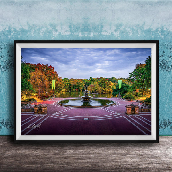 A framed photograph of a park with a fountain, surrounded by trees with autumn foliage, set against a blue wall.