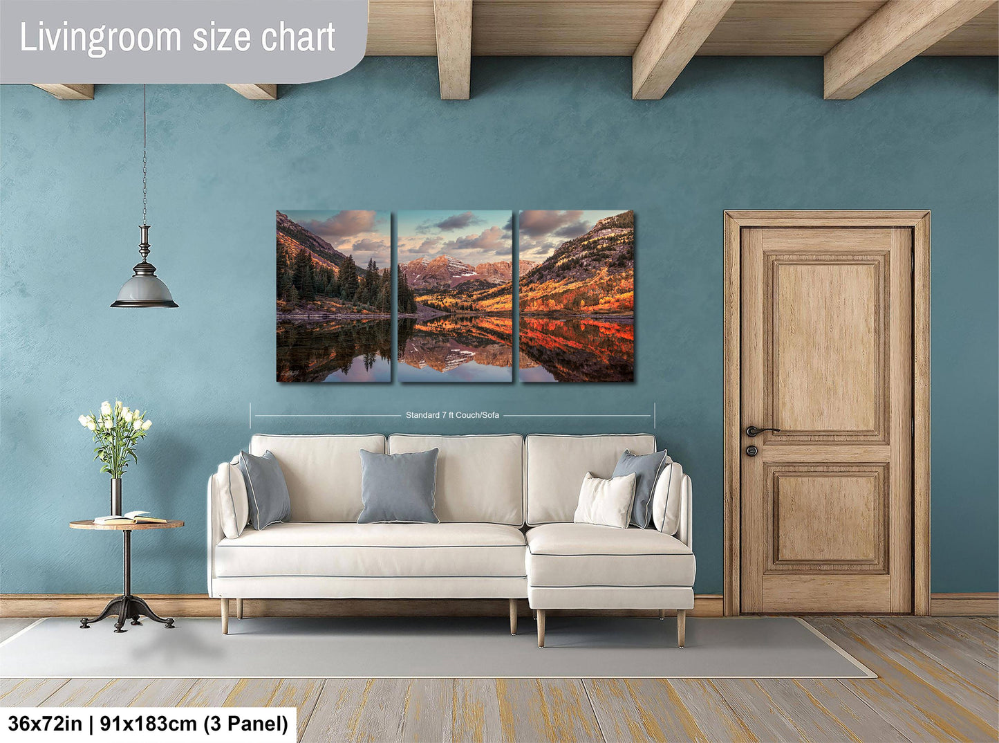 The image is a living room with a large, three-panel landscape painting hanging on the wall. The painting depicts a scenic mountain landscape with a lake reflecting the mountains. The room has a white sofa and a wooden door, creating a cozy and inviting atmosphere.