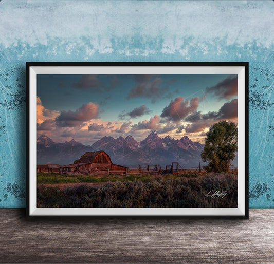 a rustic wooden barn nestled in a grassy field, with majestic mountains in the background under a vibrant sky.