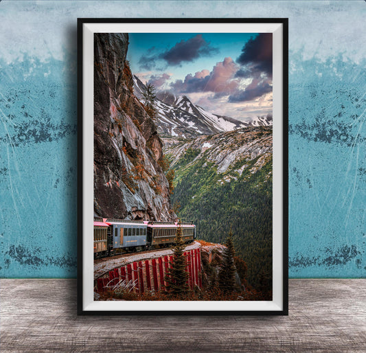 A framed photograph depicting a train traveling along a winding track that runs along the side of a steep, rocky mountain.