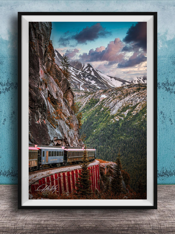 A framed photograph depicting a train traveling along a winding track that runs along the side of a steep, rocky mountain.