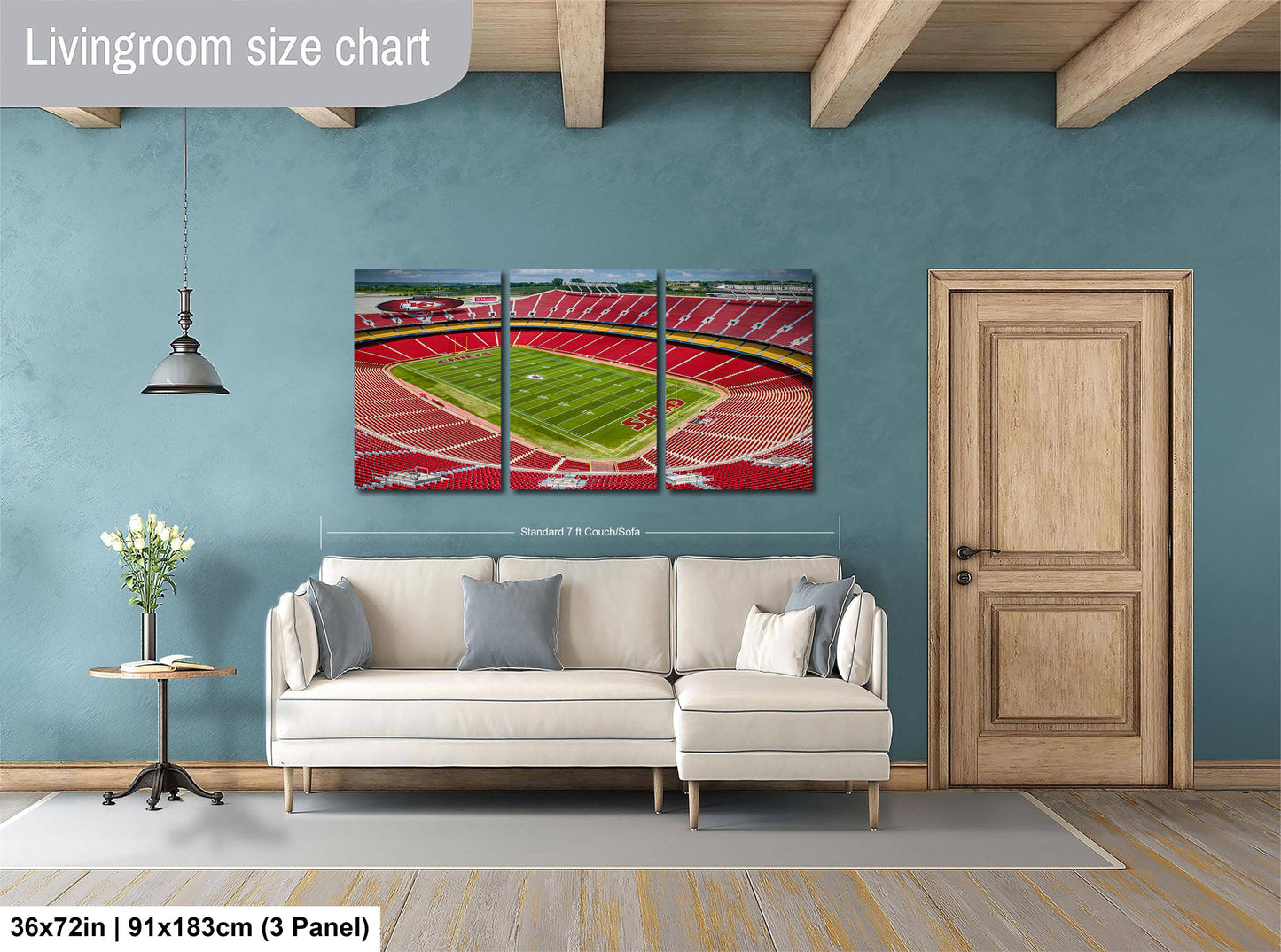 The image is a living room with a large wall-mounted painting depicting a stadium. The painting is divided into three panels, with the largest panel covering the entire wall. The room has a white sofa, a wooden door, and a small table with a vase of flowers. The painting is approximately 36 inches wide and 15 inches tall, and it is mounted on the wall above the sofa.