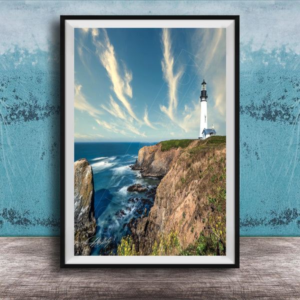A framed photograph of a lighthouse on a cliff overlooking the ocean, with a blue sky and wispy clouds in the background.