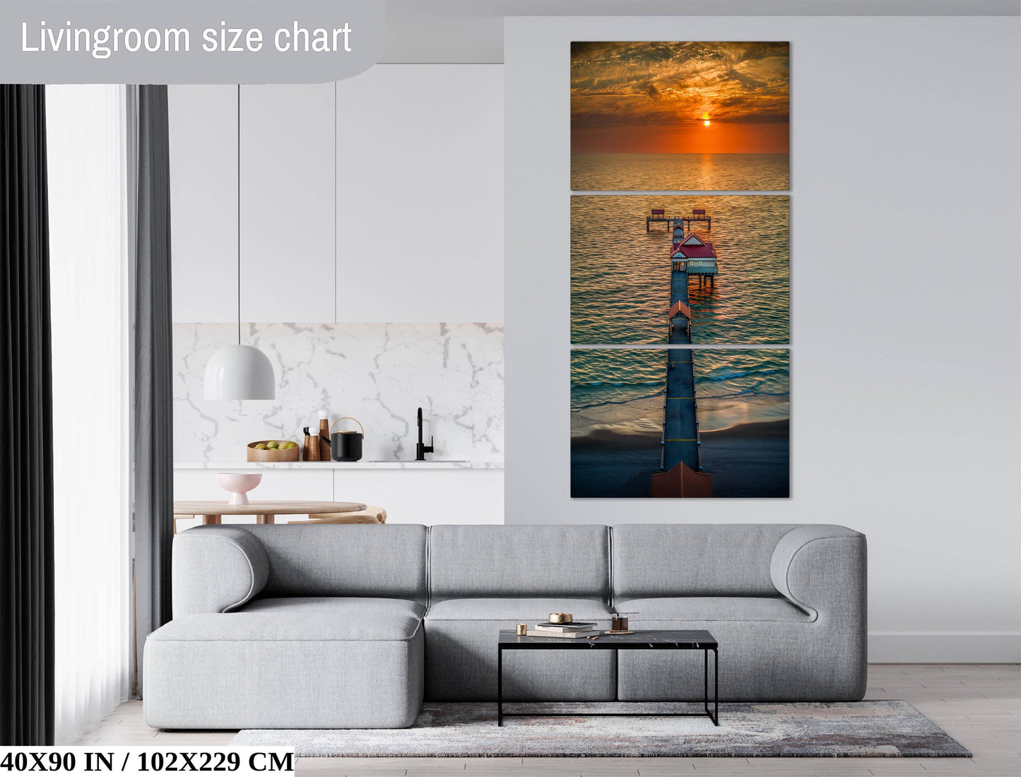 The image is a living room with a gray sofa, a coffee table, and a large wall art depicting a sunset over the ocean.