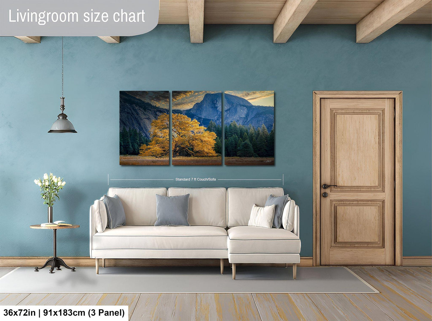The image is a living room with a large painting of a mountain landscape hanging on the wall. The painting is divided into three panels, and the living room has a white sofa, a wooden door, and a small table with a vase of flowers.