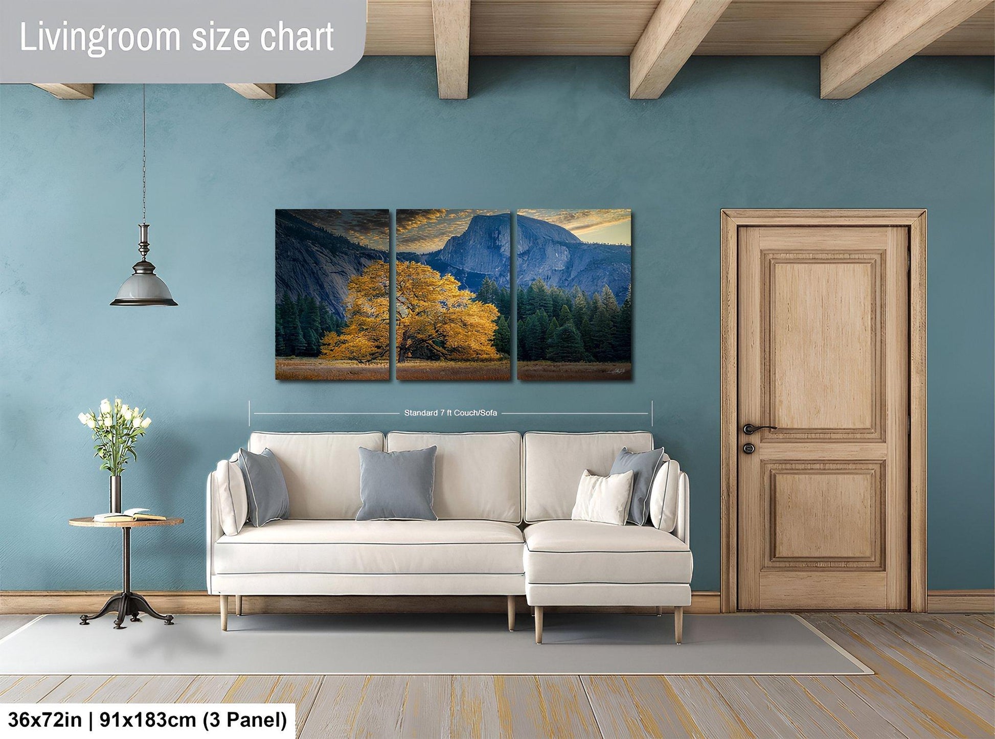 The image is a living room with a large painting of a mountain landscape hanging on the wall. The painting is divided into three panels, and the living room has a white sofa, a wooden door, and a small table with a vase of flowers.