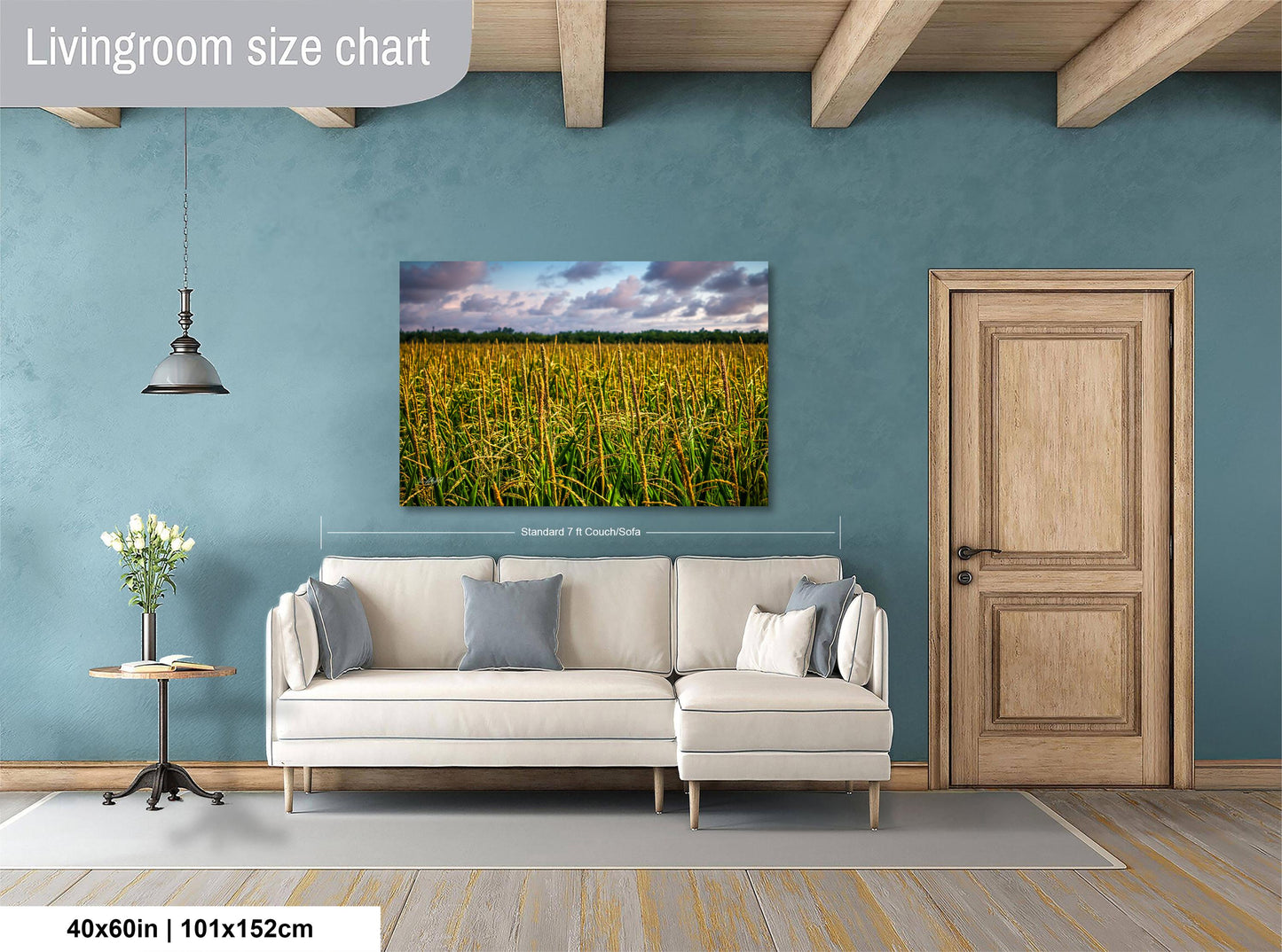 a living room with a large painting of a field of tall grass hanging on the wall. The painting is framed in a white frame and measures 40 inches by 101.5 centimeters. The room has a wooden door, a white sofa, and a small table with a vase of flowers.