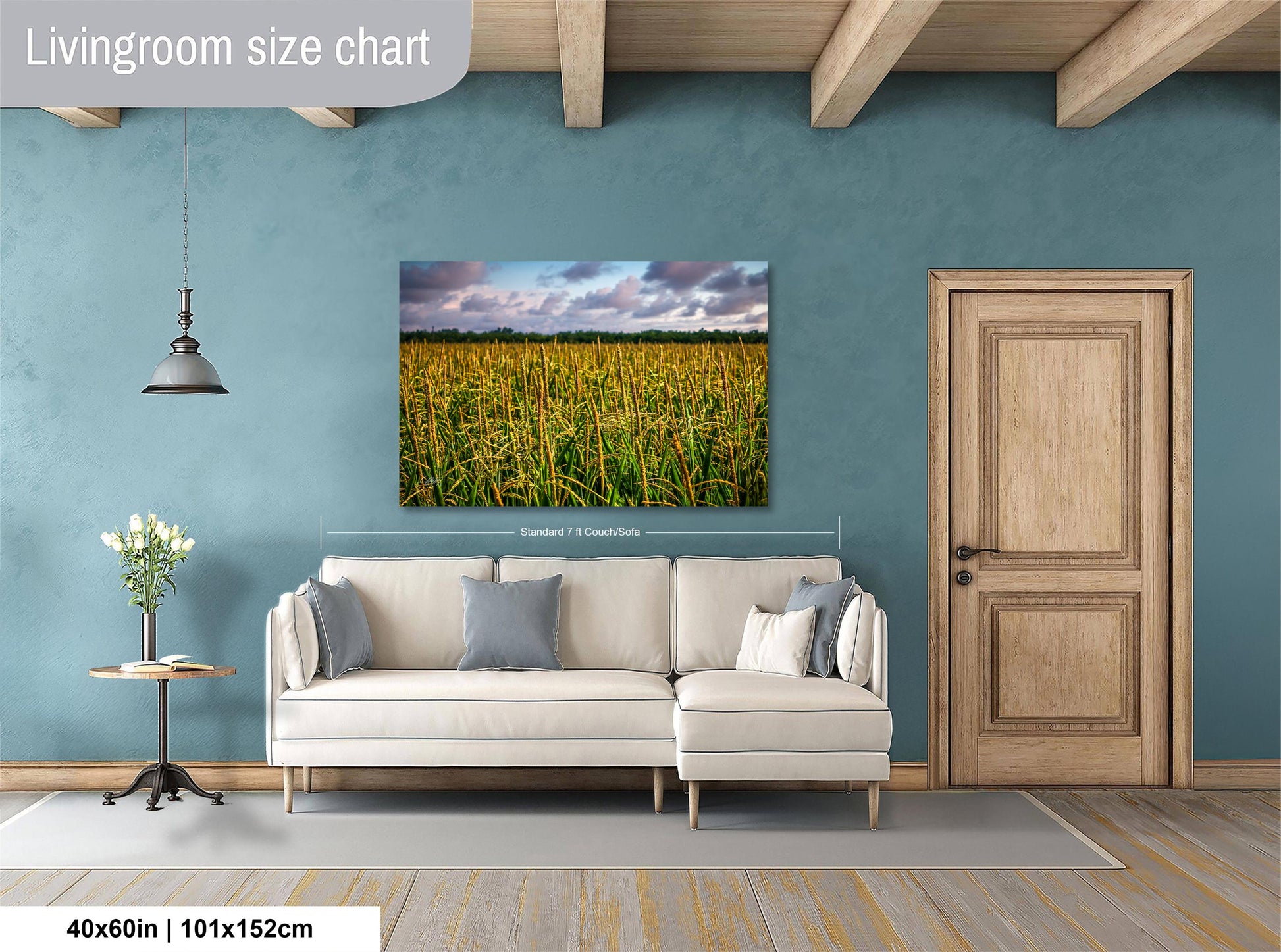 a living room with a large painting of a field of tall grass hanging on the wall. The painting is framed in a white frame and measures 40 inches by 101.5 centimeters. The room has a wooden door, a white sofa, and a small table with a vase of flowers.